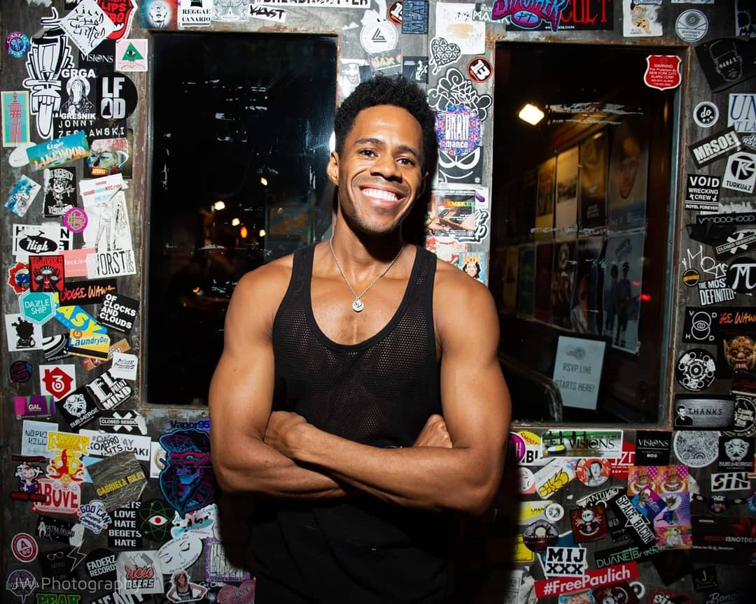 Jay Jurden with his arms crossed, standing in front of two windows that have many stickers on the wall.