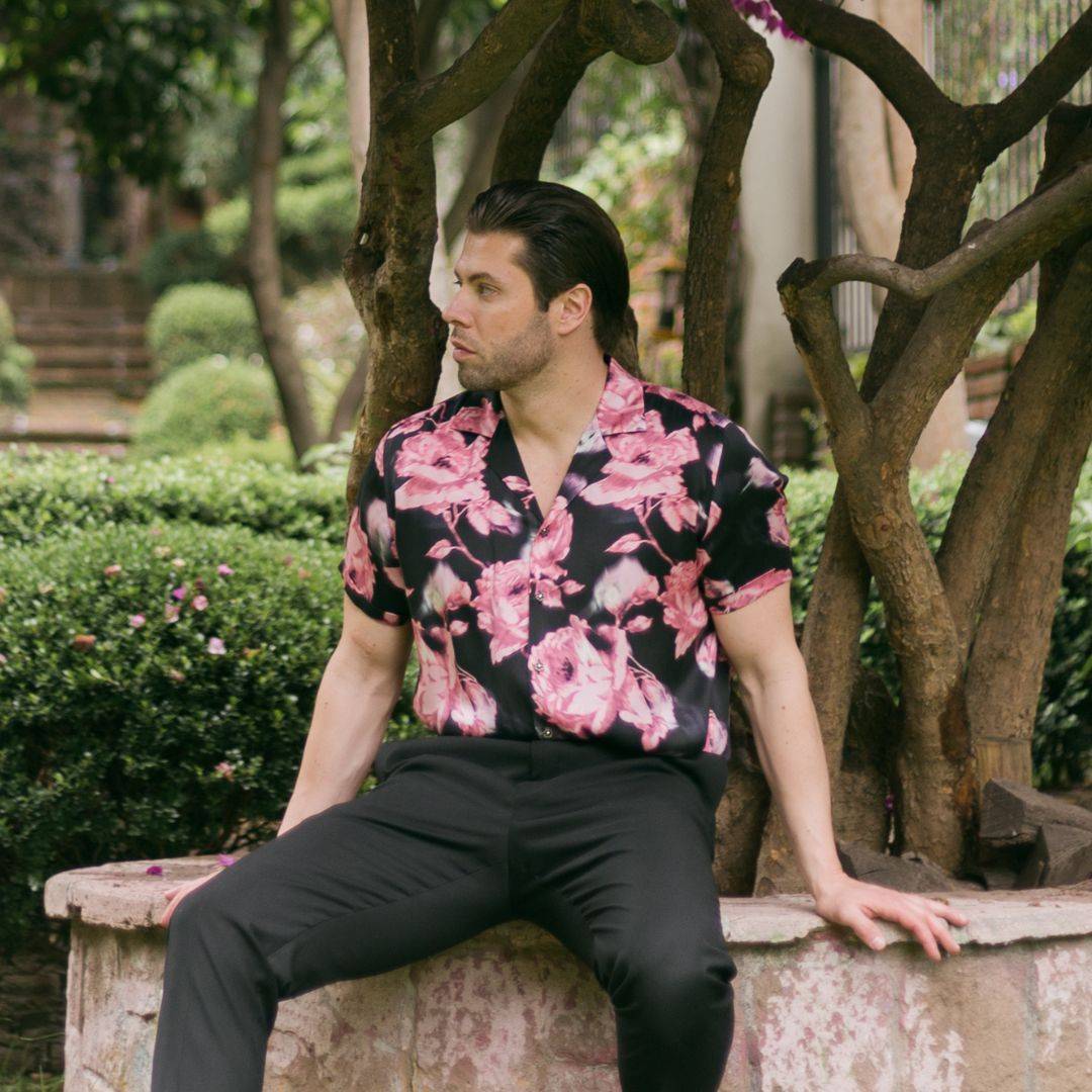 model sitting on a bench in the park wearing black pants and a short sleeve black floral silk shirt from 1000 kingdoms