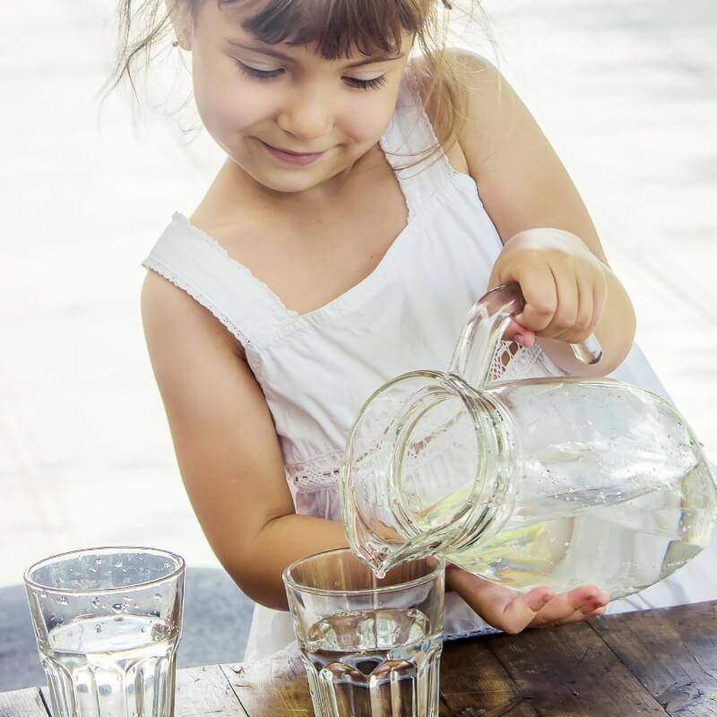 Une fille verse de l'eau dans un verre.
