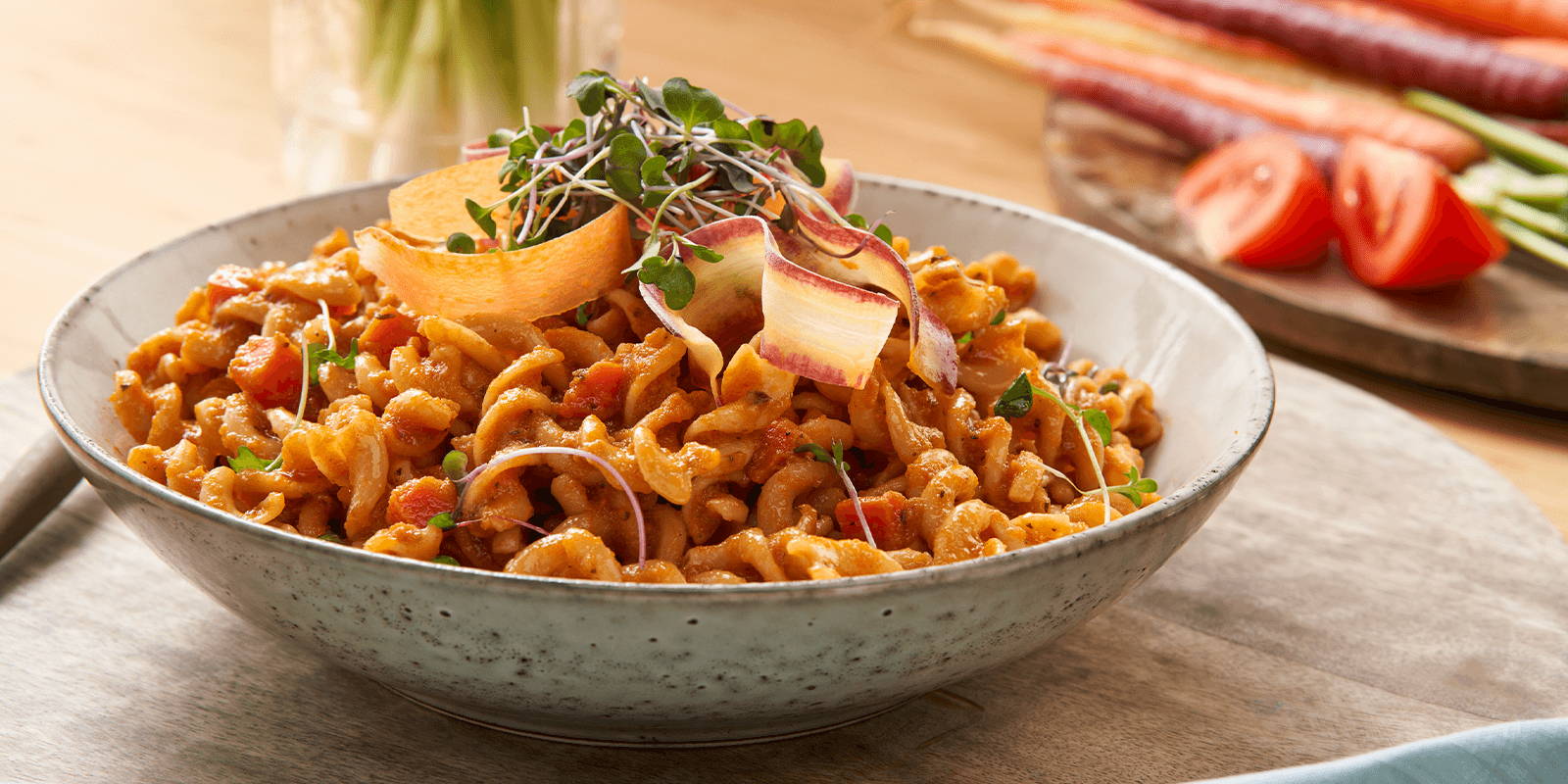 Bowl of pasta in red sauce topped with shredded carrots.