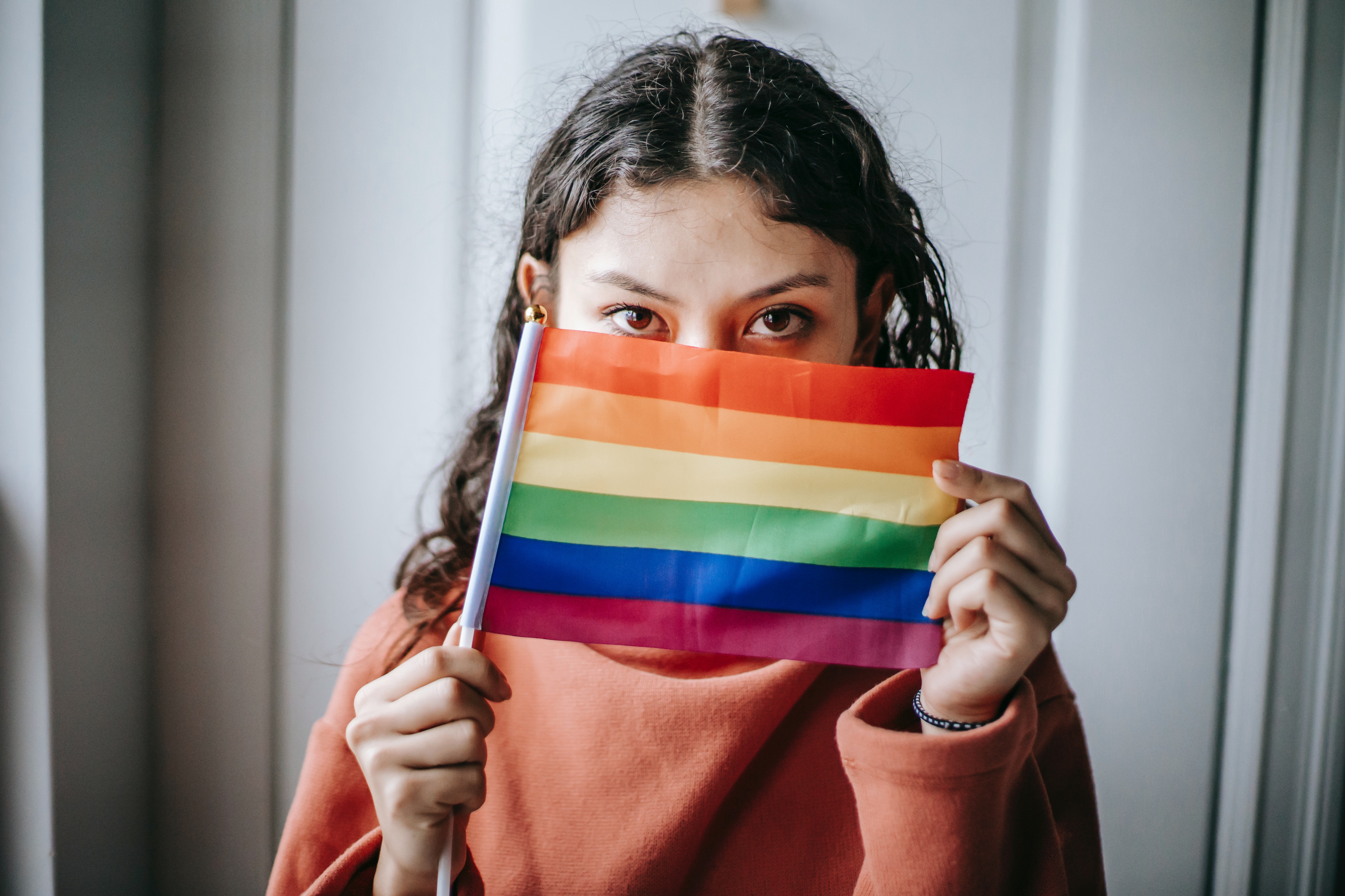 A woman with curly hair covers half her face with the pride flag.