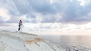 Un photographe de mariage capture le premier regard du couple sur une falaise isolée surplombant les eaux bleues claires à Paphos.