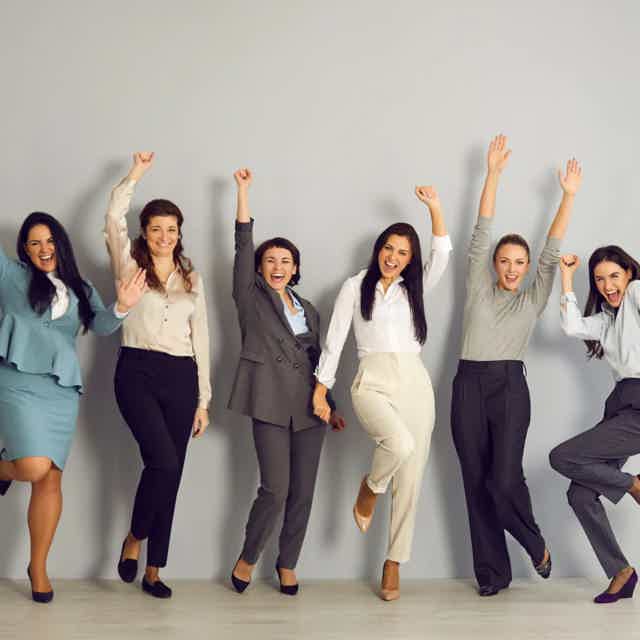 Group of diverse professionals celebrating, raising arms, smiling, and jumping in a row.