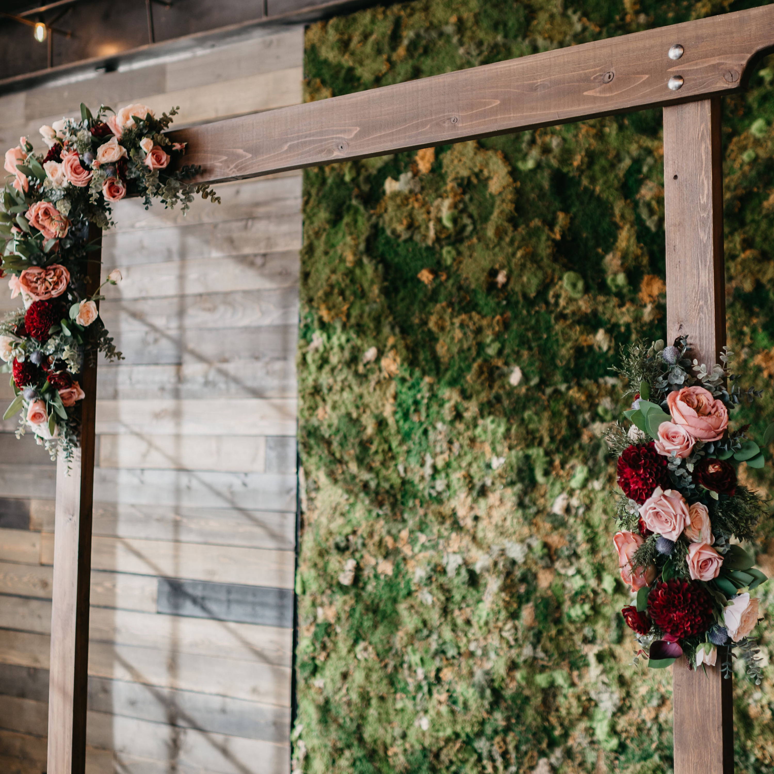 A square wedding arch adorned with 2 floral pieces with burgundy and blush flowers 