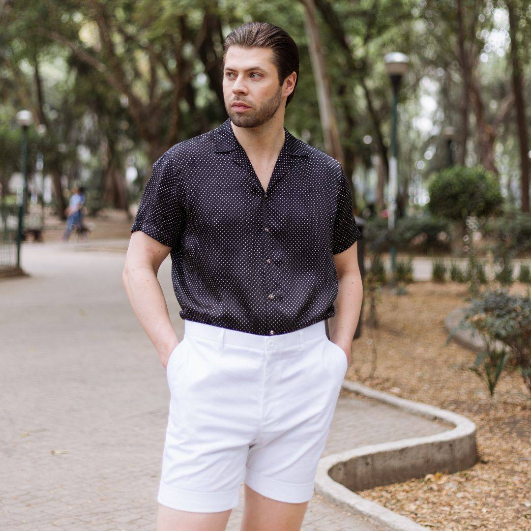 model standing in the park and wearing white shorts with a short sleeve black dotted silk shirt from 1000 kingdoms