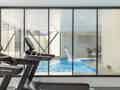 Ein moderner Fitnessraum mit Laufbändern, die auf ein Hallenbad mit Wasserspiel und Liegestühlen blicken.