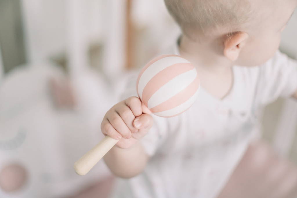 Baby holding a pink/white rattle toy.
