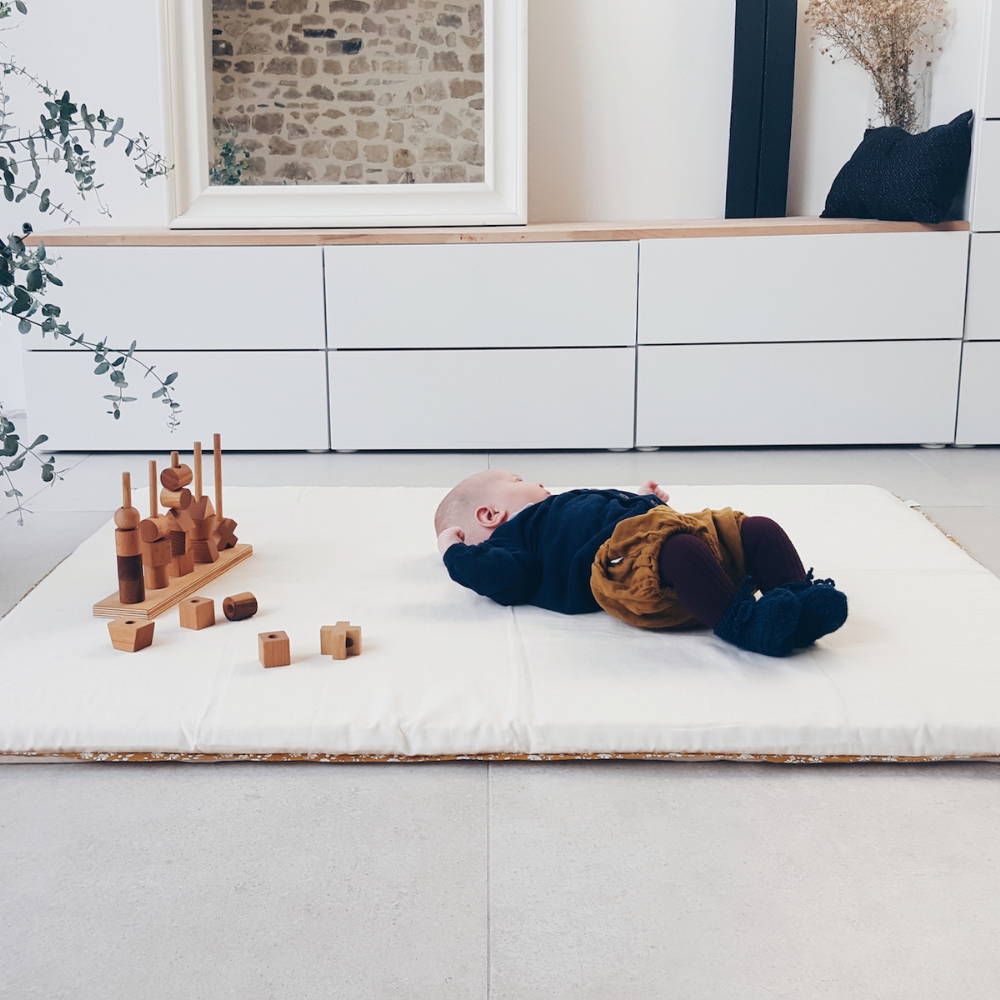 Enfant allongé sur un tapis avec un jouet Montessori