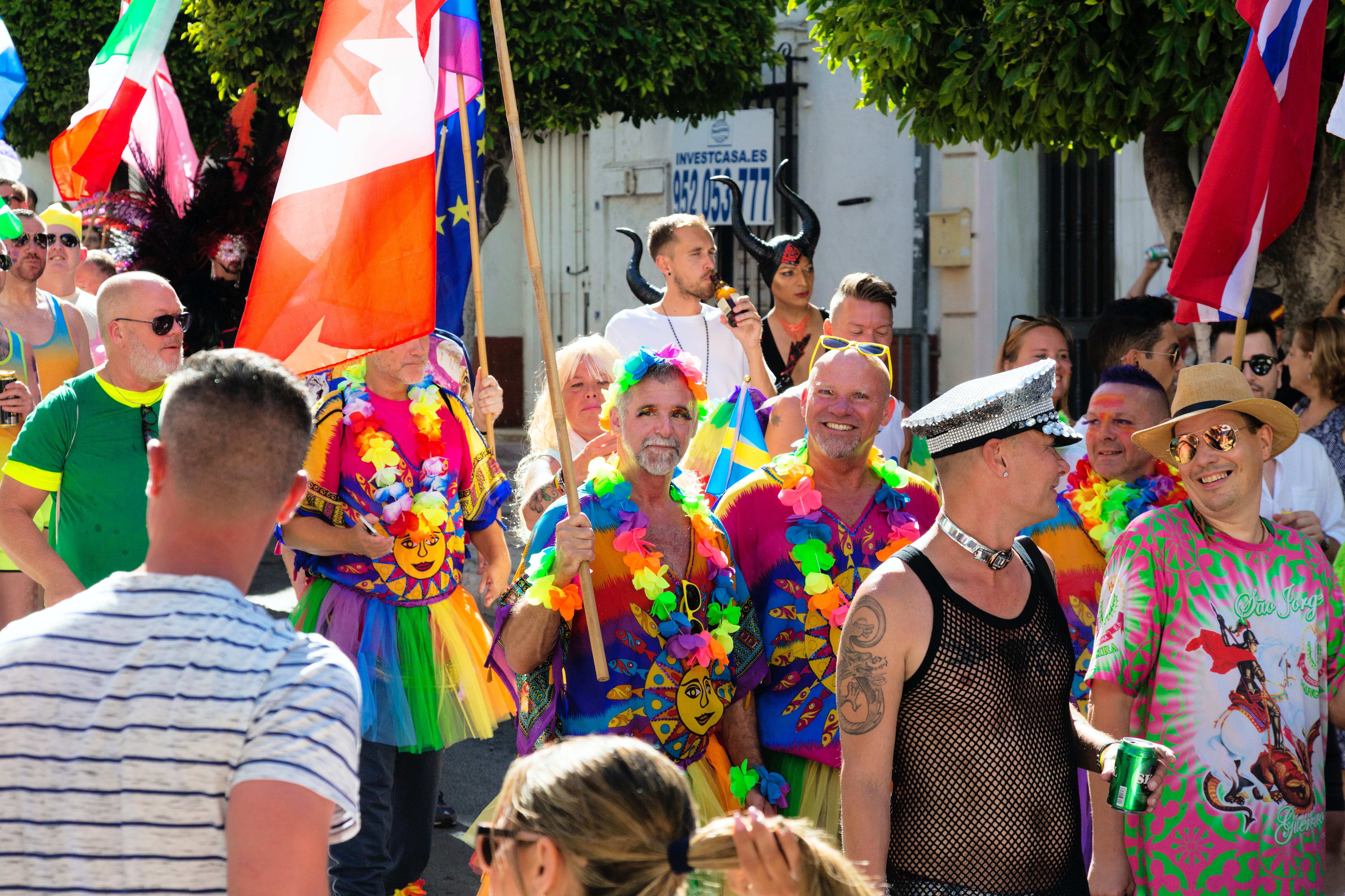 A pride march where there is a lot of people mainly older men wearing colorful outfits all smiling.