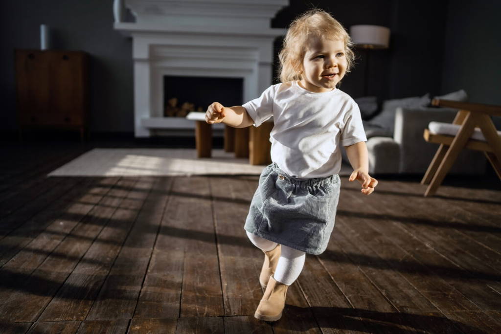 Blonde toddler running in a dark living room.