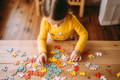 Girl playing with puzzles on a wooden table. 