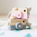 A pink Montessori Wooden Camera with an adjustable strap and a shutter button sitting on top of a gray wooden camera. 