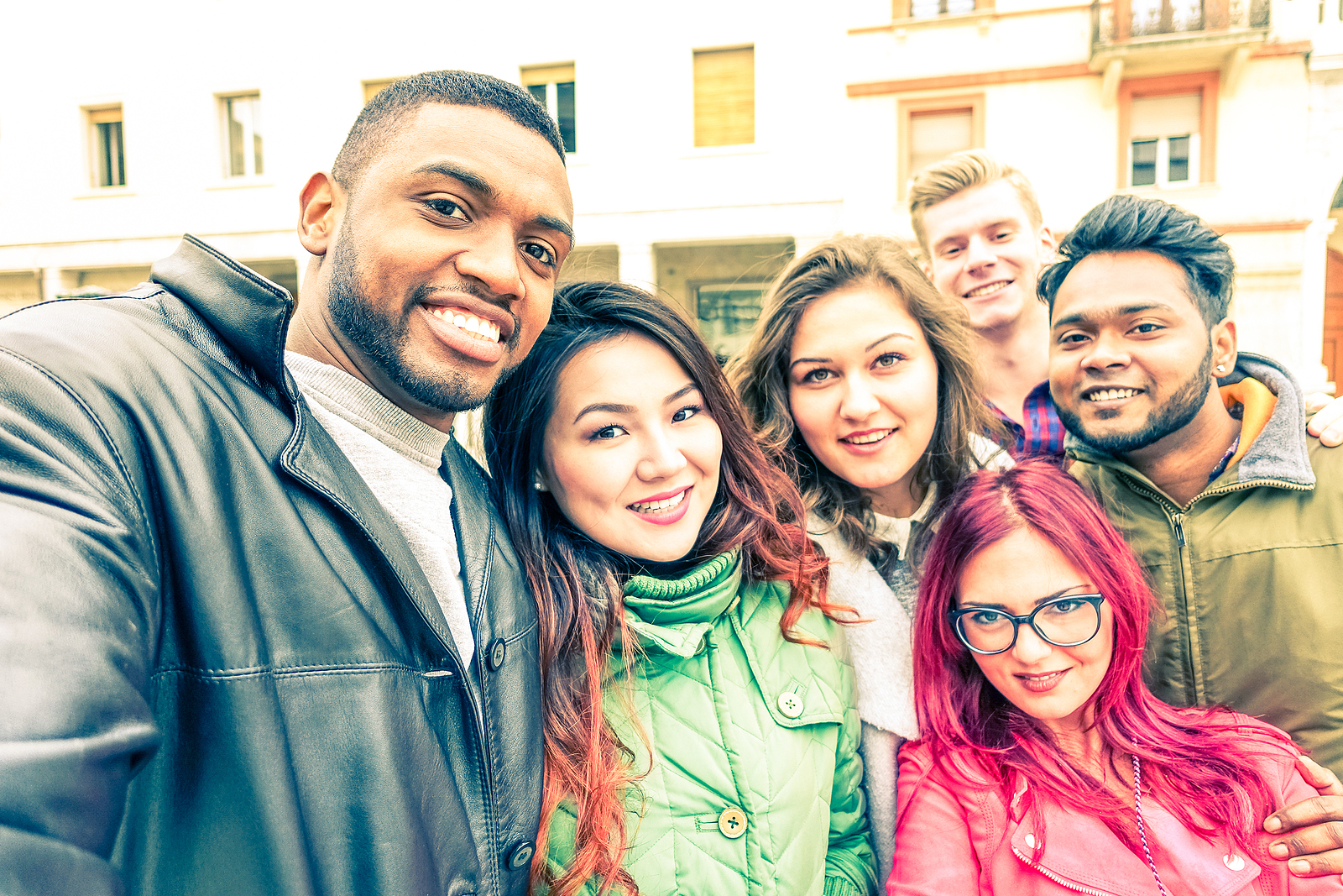 Image of a multiracial group of 6 friends dressed for the winter, all taking a selfie in the street smiling.