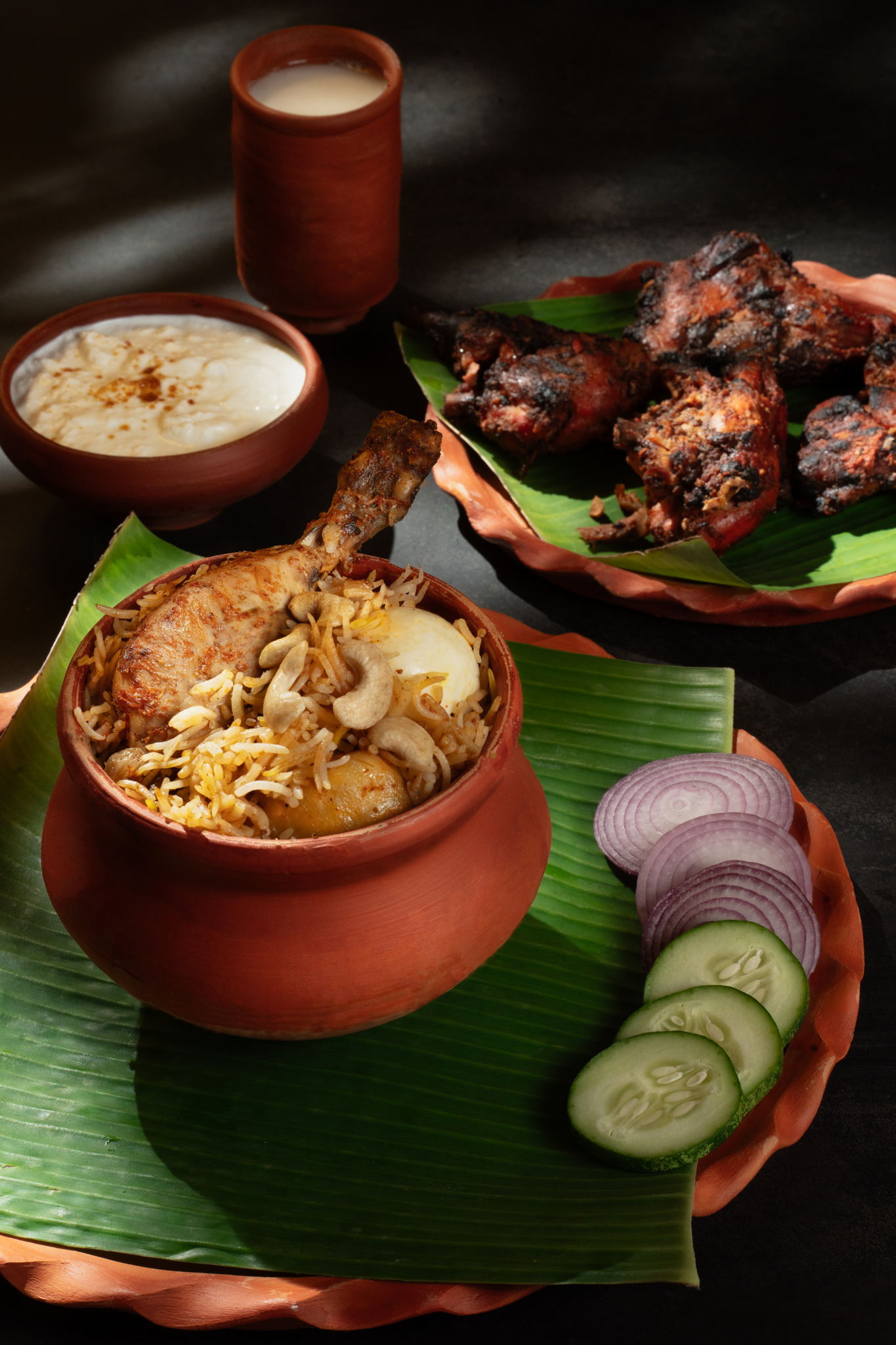 Close-up of a traditional Indian chicken biryani dish on a banana leaf, garnished with onions, cucumbers, and yogurt