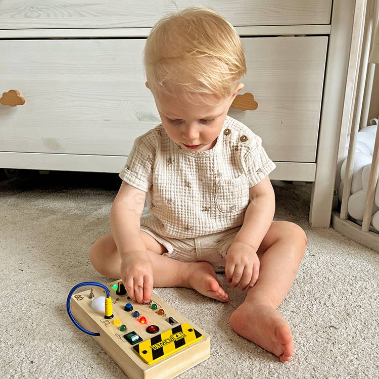 Blonde toddler sitting on the carpet and playing with a Montessori Switch Board.