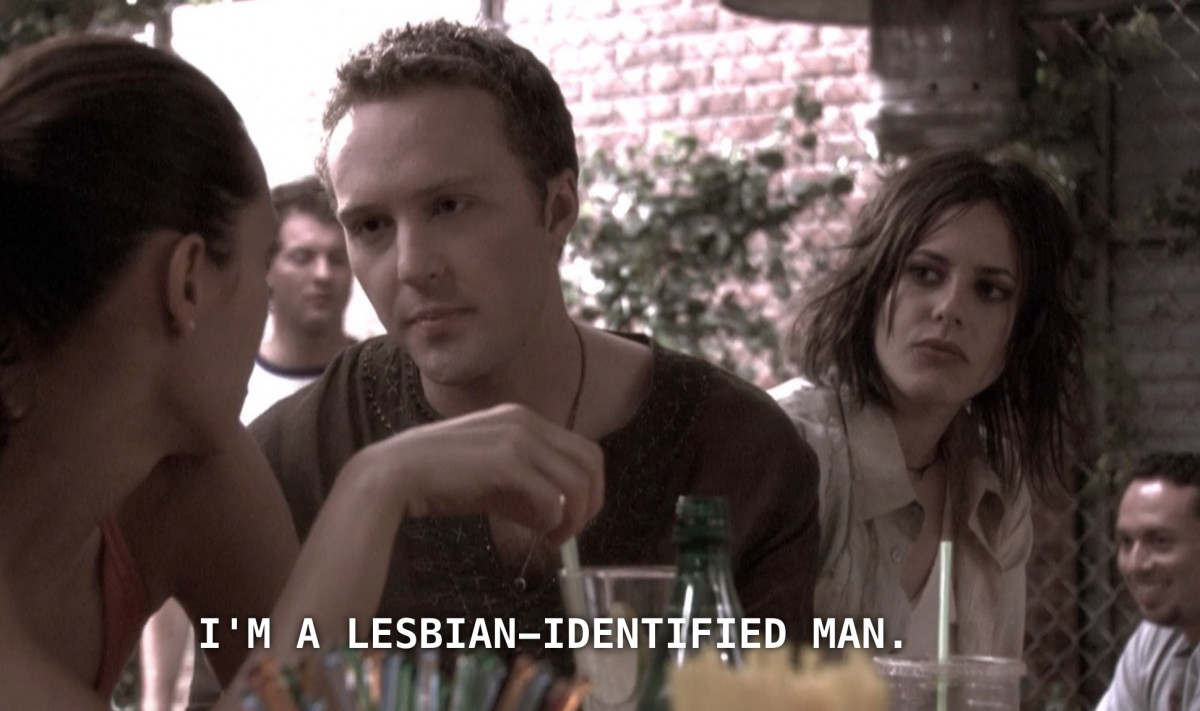 Shane watching a couple talking with concern. The subtitles underneath says I'm a lesbian identified man.