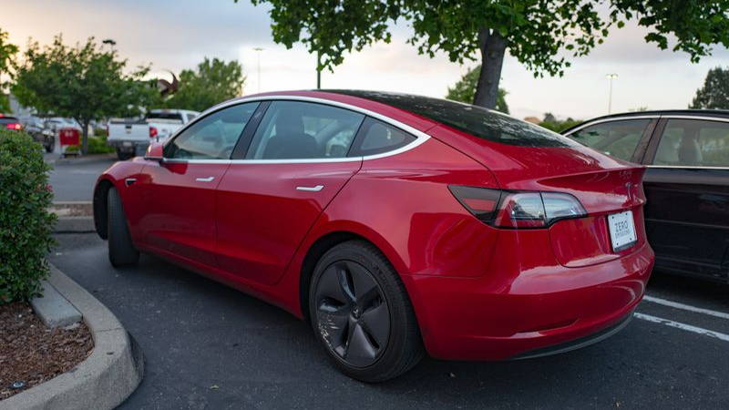 Side view of a red Tesla Model 3 electric car from Tesla Motors under a dramatic sky in the San Francisco Bay Area, Dublin, California, May 21, 2018.