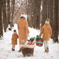 Mother and daughters in matching coats walking down a snowy road and pulling sleds.