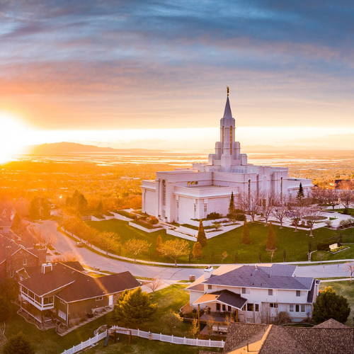 Photo of the Bountiful Temple next to a sunburst just above the mountains. 