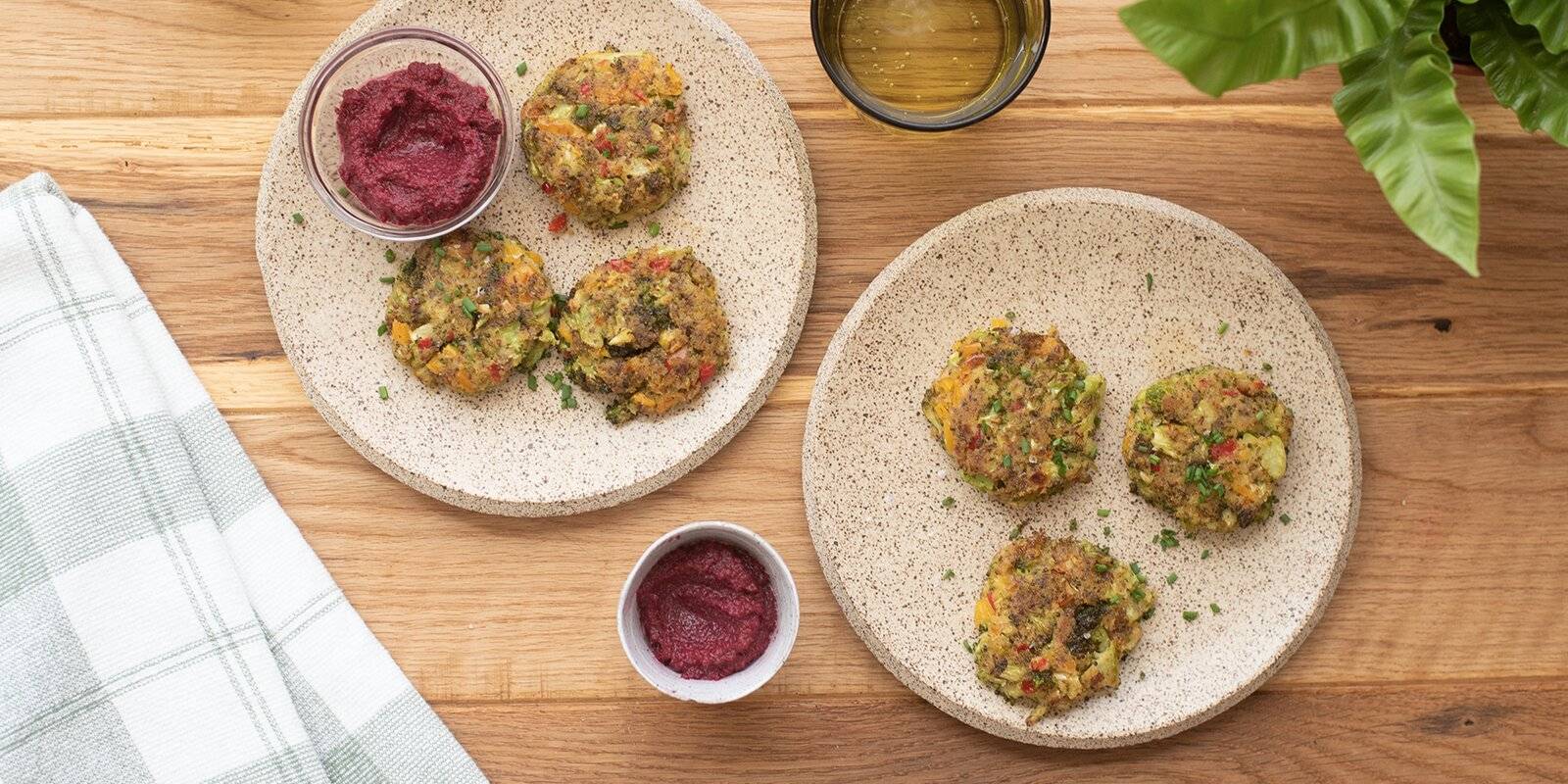 Two plates of veggie nuggets alongside two containers of beet dip. 