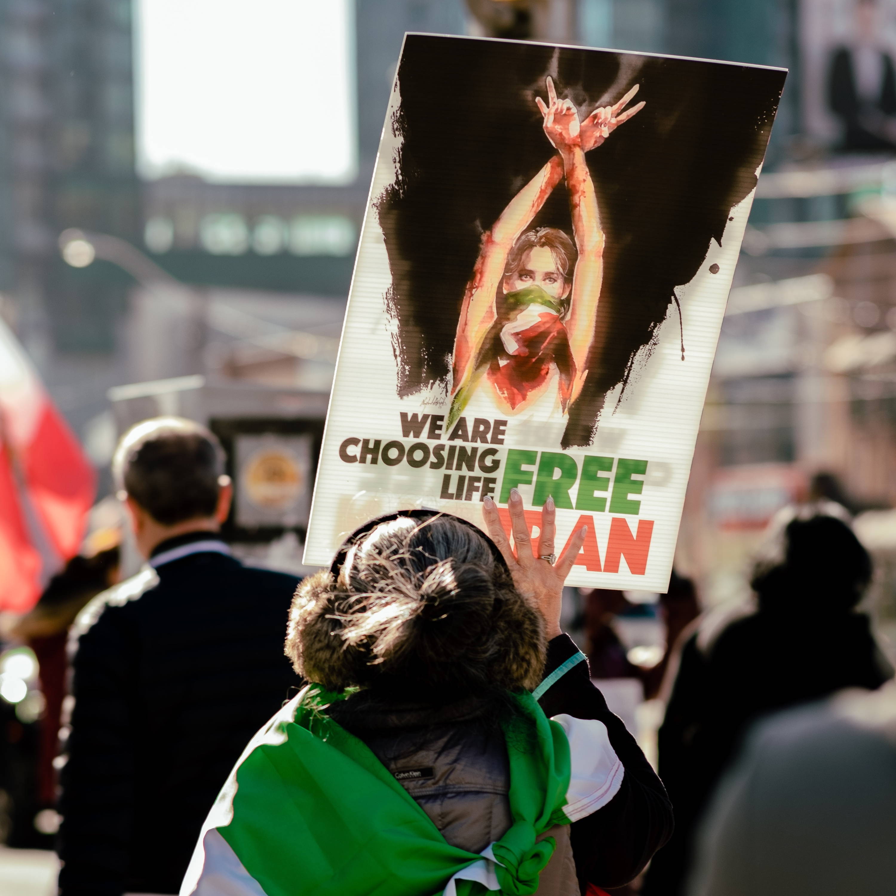 A woman protests Iran regime with a sign reading "We are choosing life. Free Iran."