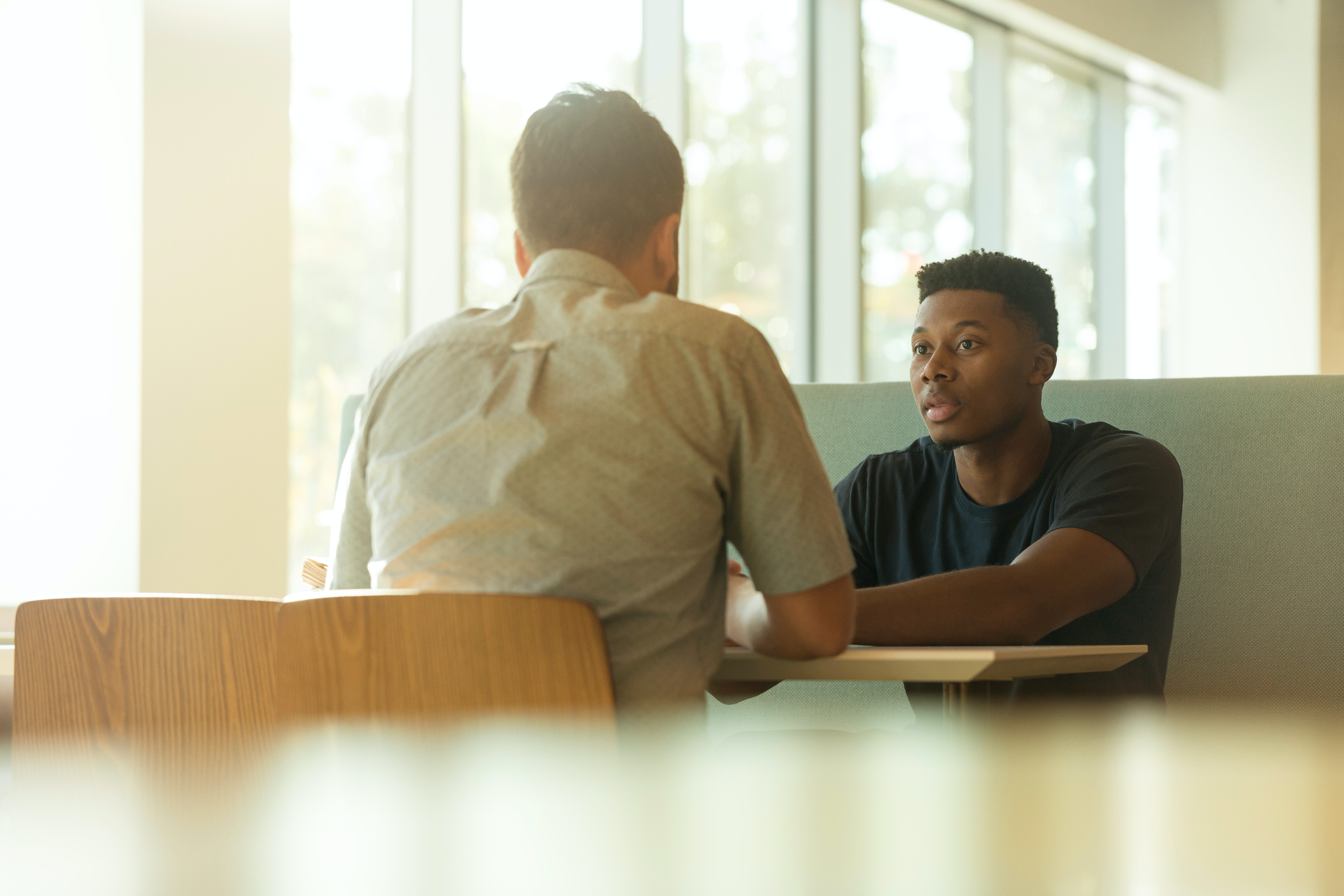 A black and white guy sitting at a table together, having a deep conversation.