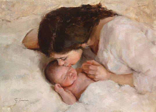 A mother lying in a white bed kissing her infant's head. 