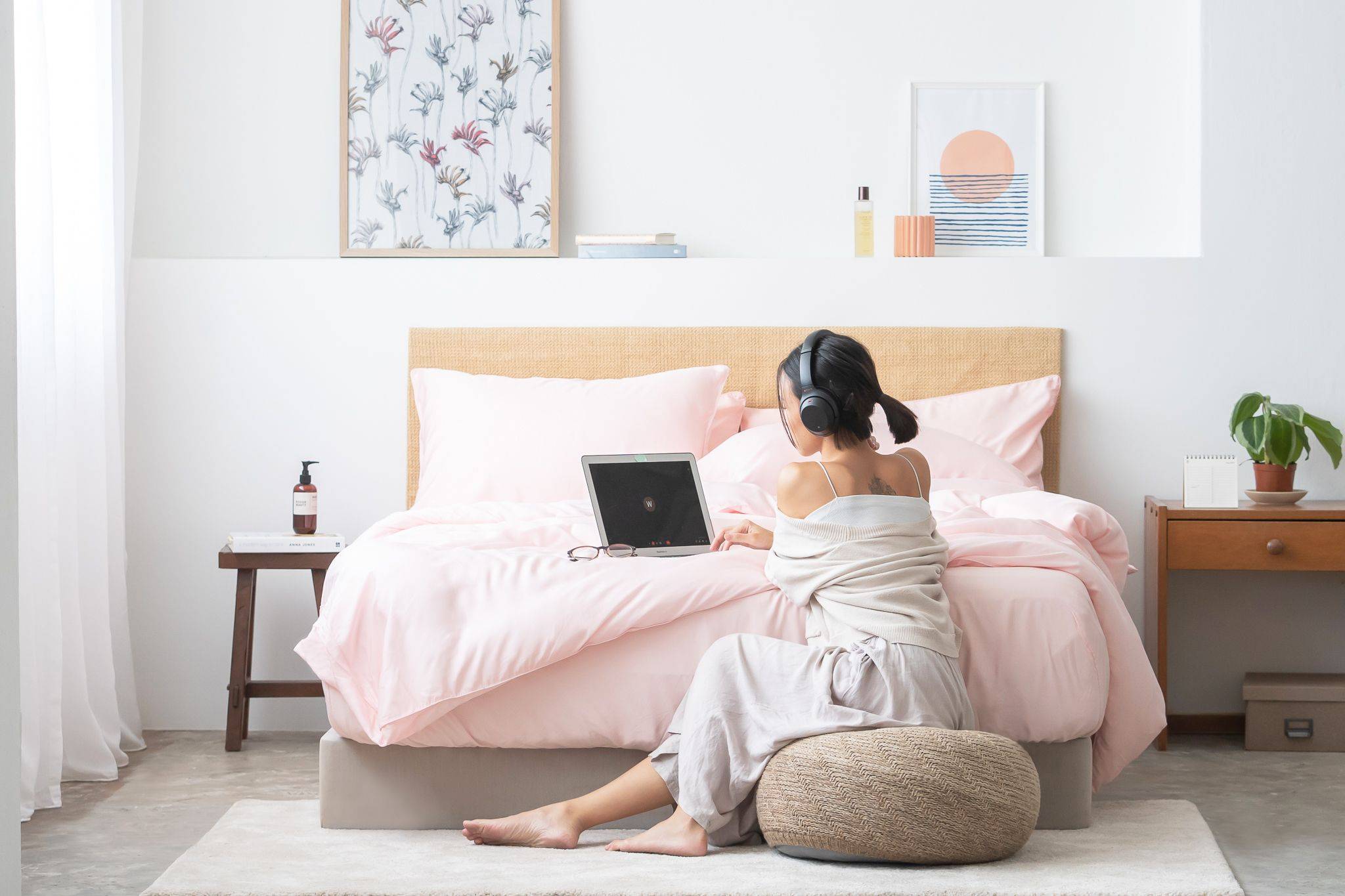 Girl using laptop with headphones on Weavve's tencel lyocell pink bed sheets