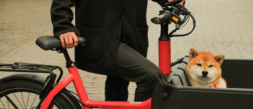 a woman standing next to a red electric cargo bike with a dog in the front carrier