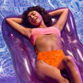 woman lounging on purple pool float in pool wearing pink and orange bikini