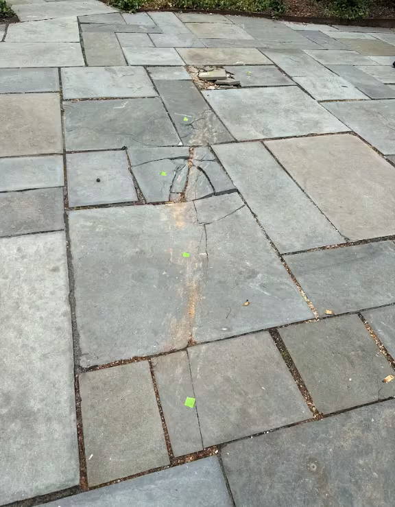 A smiling technician in a gray uniform standing in front of a cracked concrete patio, representing repair services.