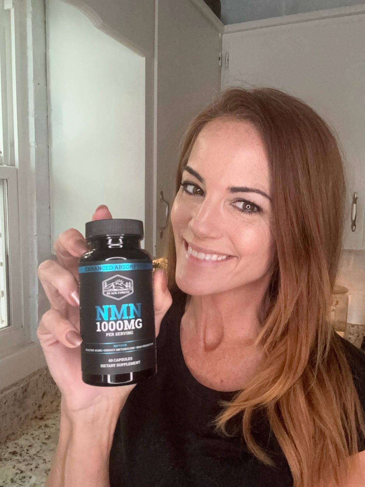 An early 40s smilling woman with a bottle of Black Forest NMN