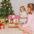 Sisters playing with a pink dollhouse next to a Christmas Tree.