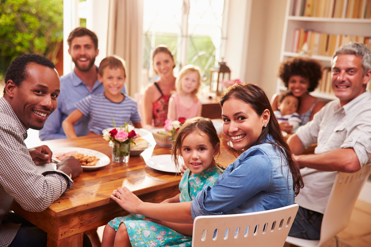 A large multi ethnic family sits a the table all turned around looking at you and smiling.