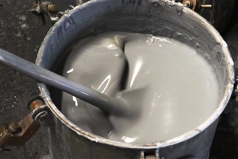 A bucket of grey liquid vitreous enamel is being stirred