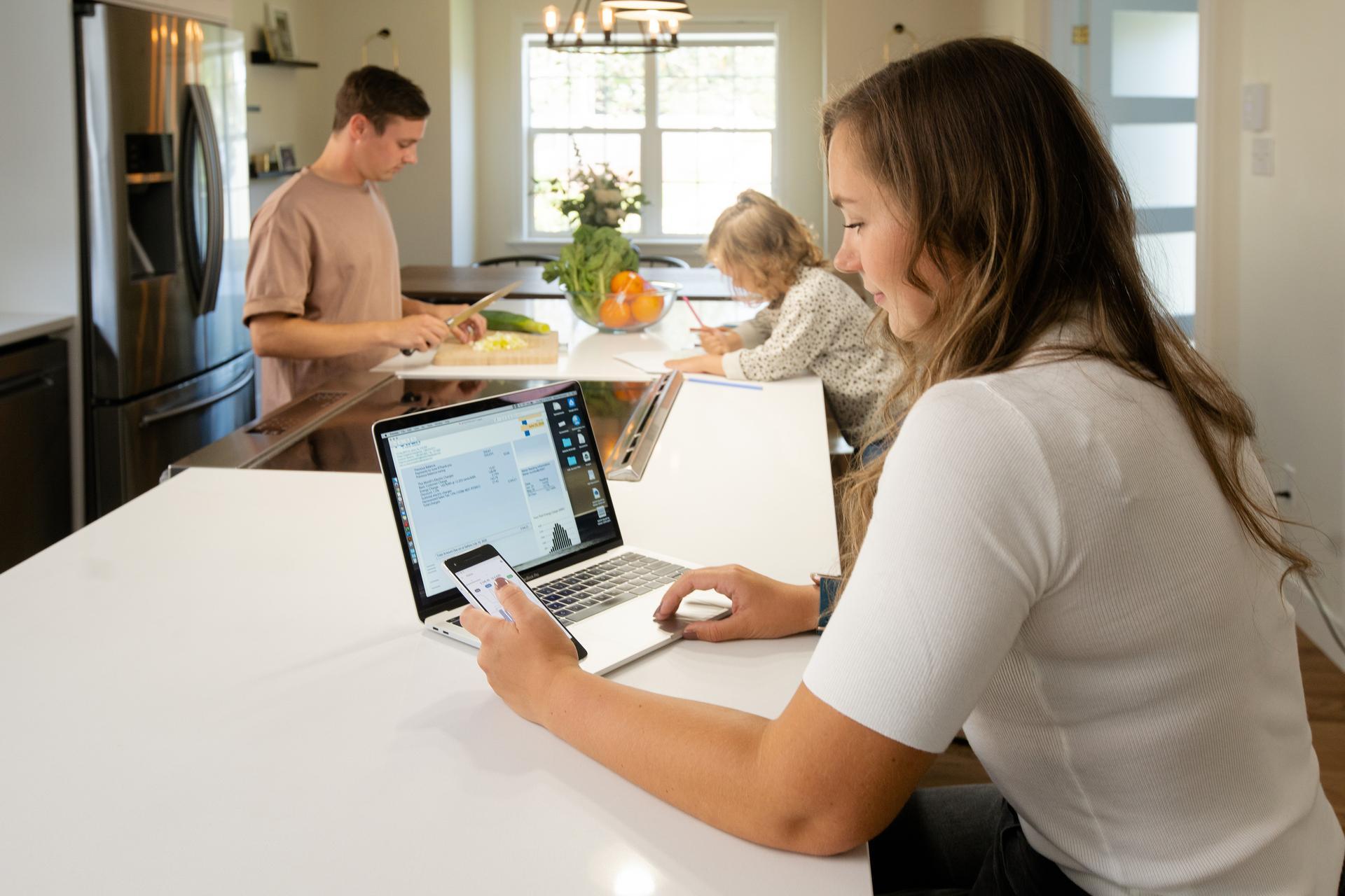 mother sitting at kitchen island using smart ac app while father and daughter prepare dinner