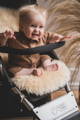 A smiling blond baby sat on a long haired sheepskin liner in a mountain buggy pram