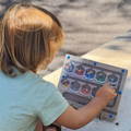 A child using a magnetic pen to guide colorful balls into their color matching containers inside a wooden maze.