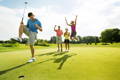 Happy golfers jumping and celebrating a successful putt together on the green.