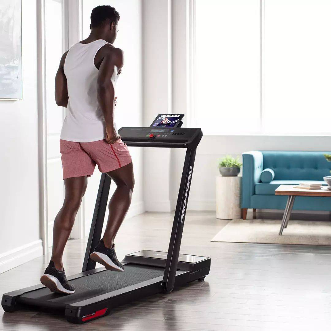 athlete in white shirt and pink shorts running on PROFORM CITY L6 treadmill at home in front of a blue sofa