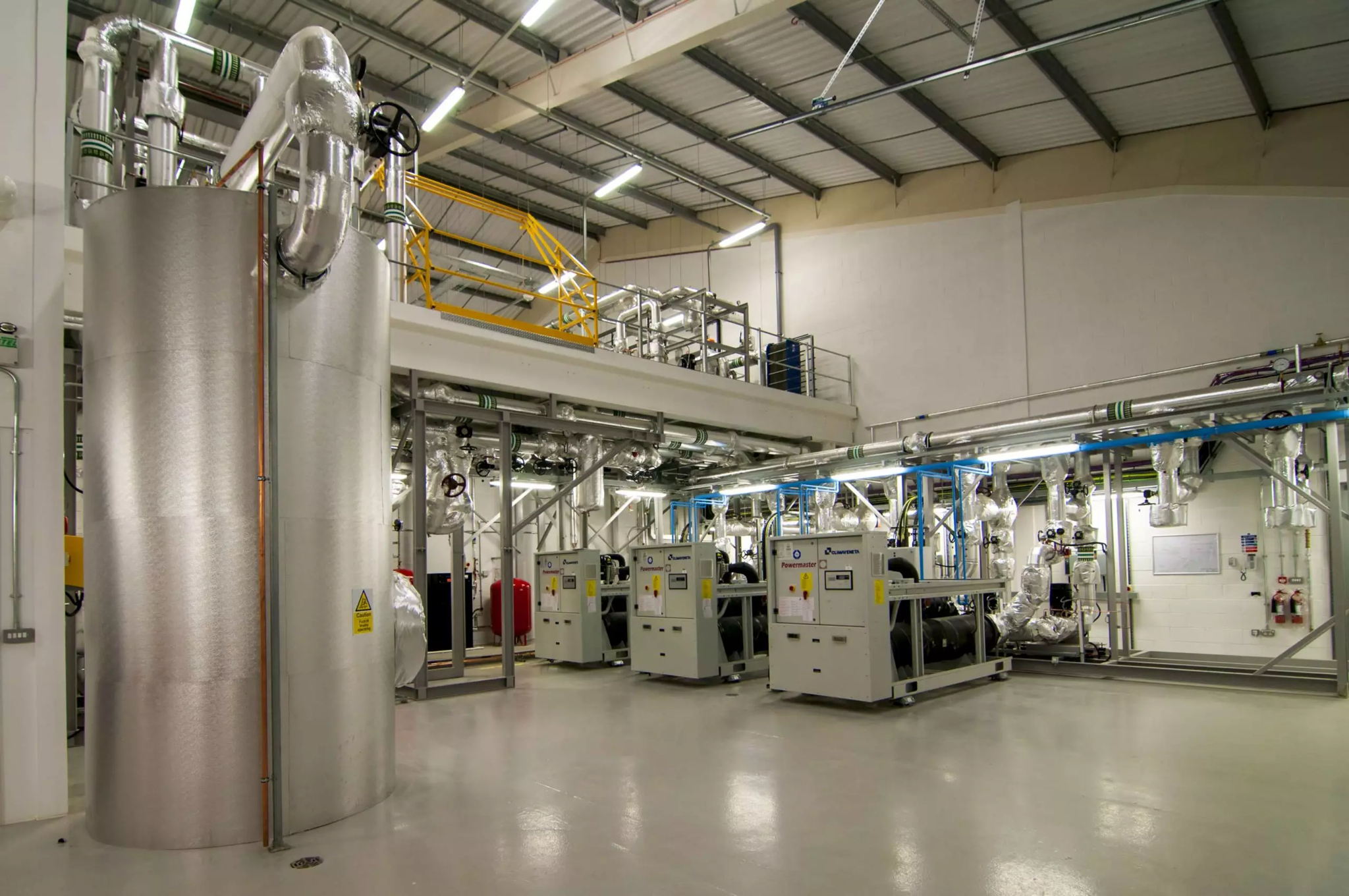 A modern industrial facility interior with large metal tanks, machinery, and pipes, featuring a clean and bright environment with high ceilings and exposed beams.