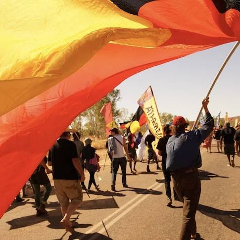 Freedom March retracing Wave Hill Walk-off with people marching with Aboriginal flag