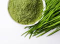 aerial view of a bowl of green powder next to fresh wheat grass clippings