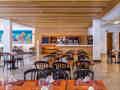 Modernes Hotelrestaurant mit Holztischen, schwarzen Stühlen und einem Selbstbedienungsbereich für Kaffee.