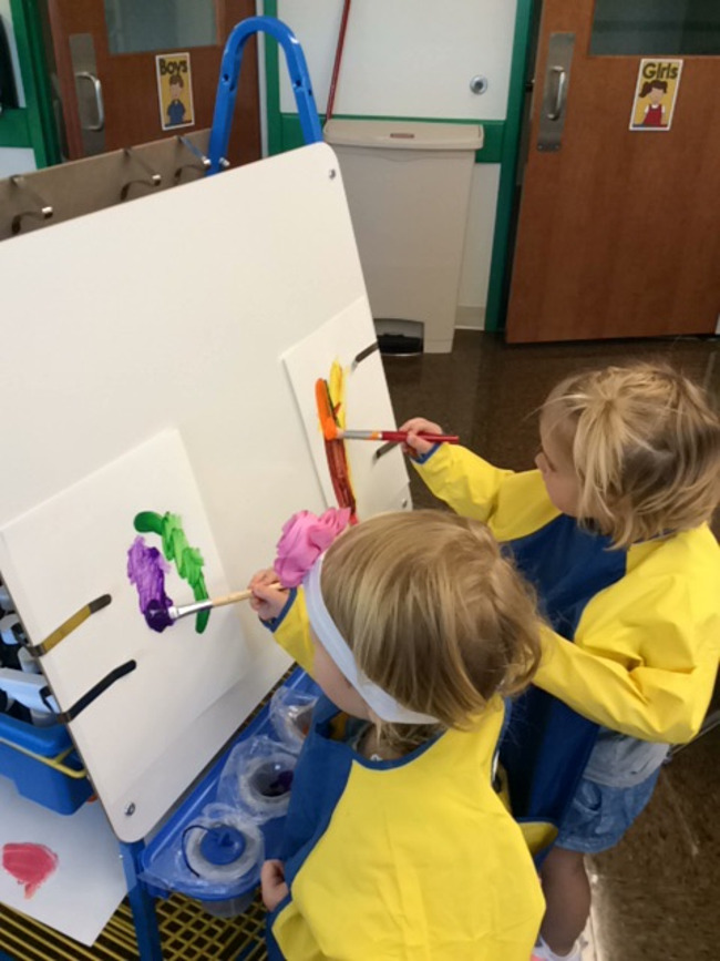 Two young Primrose students paint on canvas mounted on a stand