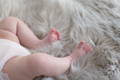 A baby's legs laying on a grey long haired sheepskin