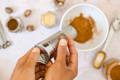 Whole nutmeg is being ground into a white bowl surrounded by glass spice jars