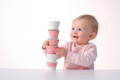 Cute baby in a pink shirt holding cups that are stacked on top of each other.