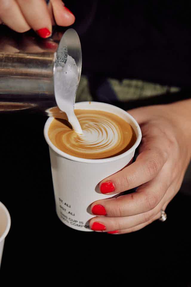Barista pouring milk into coffe as a pattern in a takeway cup