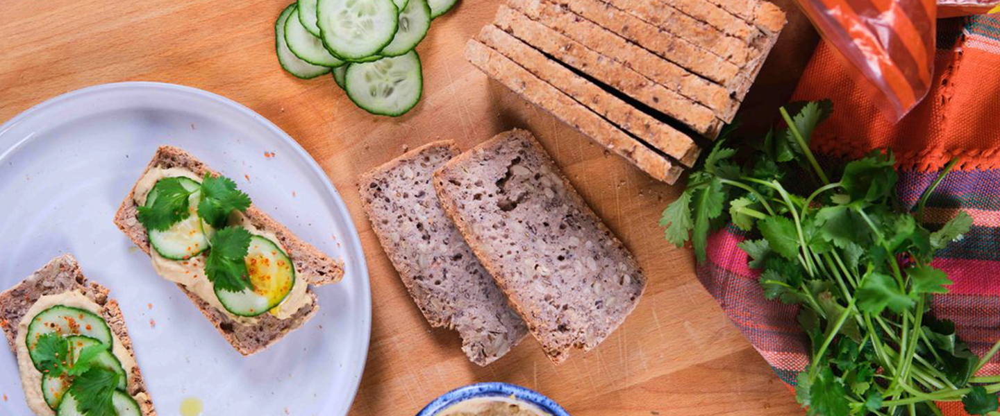 PACHA sprouted buckwheat bread slices served with hummus, cucumber, cilantro, and fresh ingredients on a wooden kitchen board